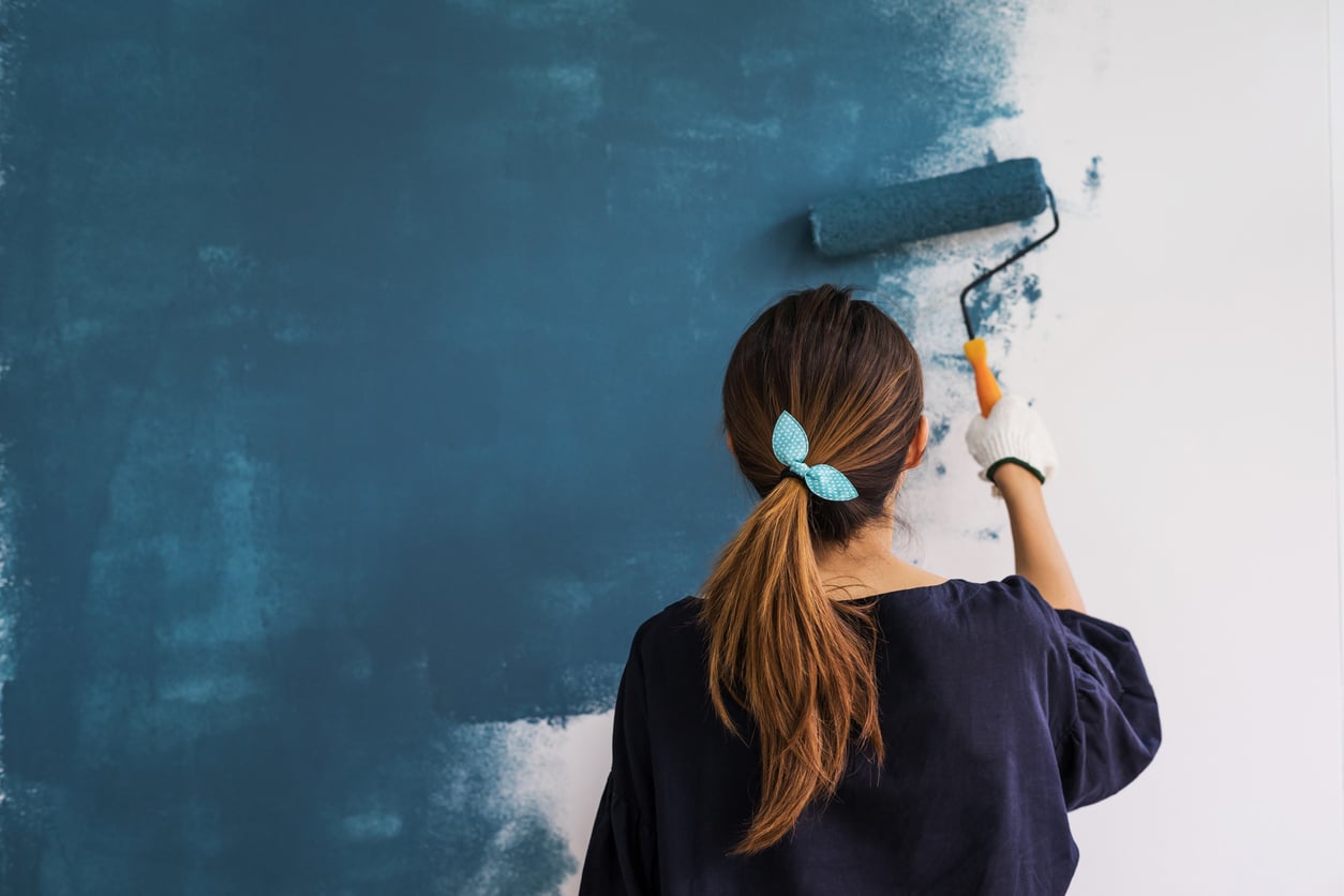 Young asian happy woman painting interior wall with paint roller in new house