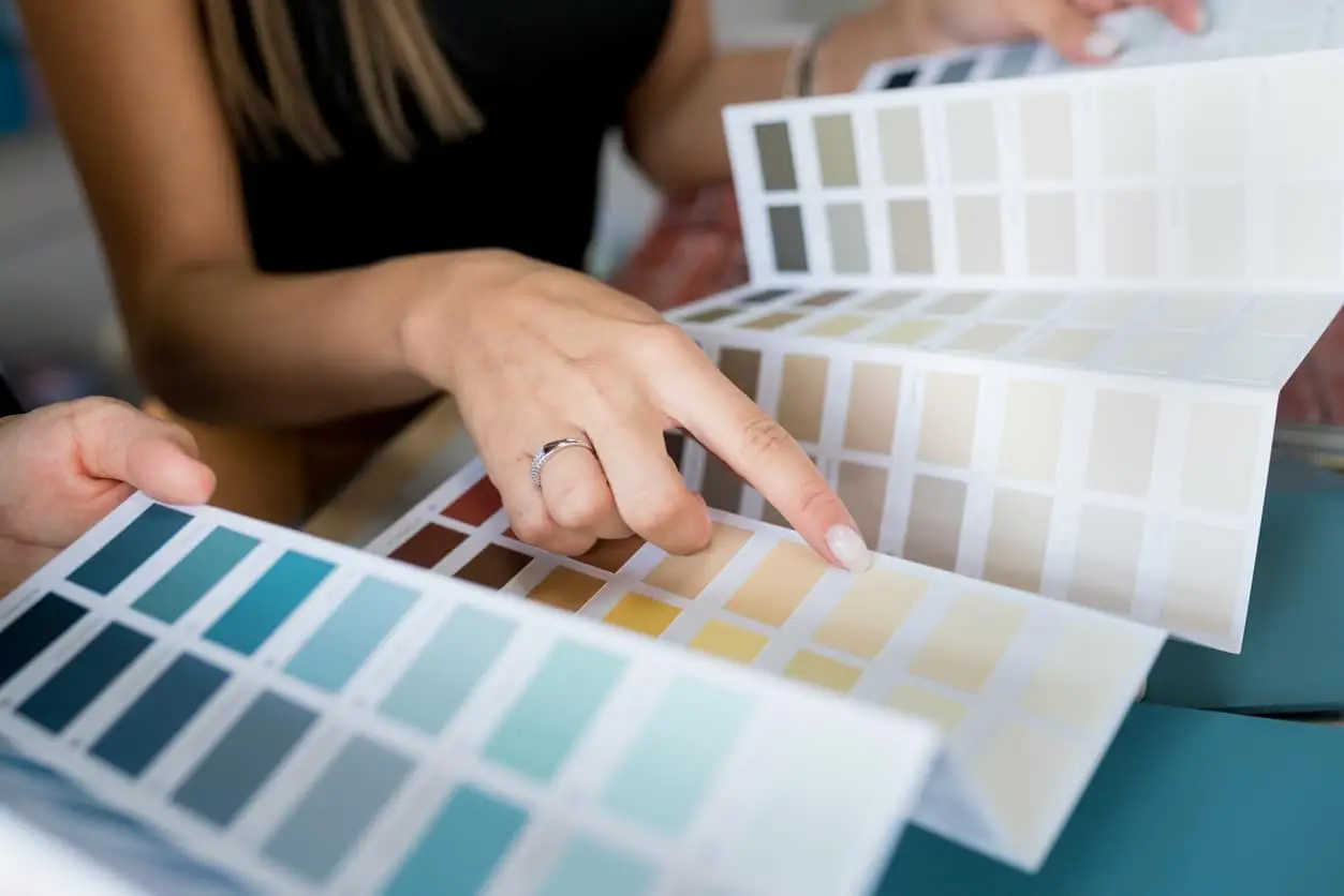 Close-up of two women choosing samples of wall paint. Interior designer consulting a client looking at a colour swatch. House renovation concept