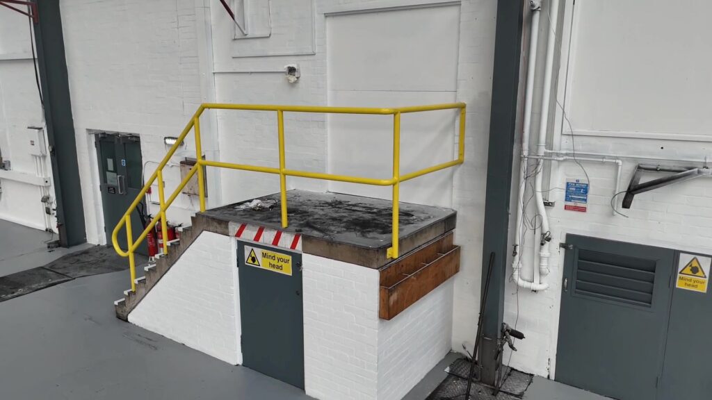 Freshly painted commercial interior in Leicester with clean white walls, grey flooring, yellow safety rails, and clear signage by professional painters