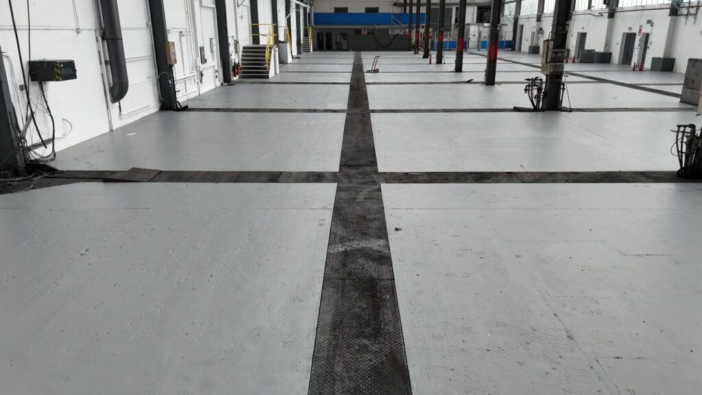 Commercial warehouse interior featuring freshly painted concrete floors with visible dark anti-slip safety strips, completed by painter and decorator in Leicester.