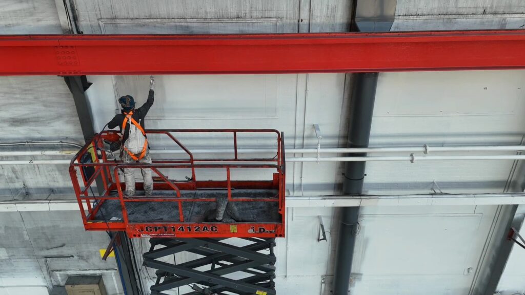 Commercial painter in Leicester on a scissor lift painting high warehouse walls and steel beams for industrial property maintenance