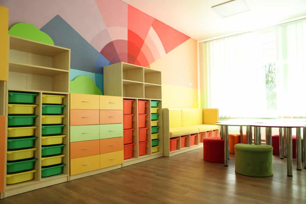 Desks, chairs and shelving unit near bright wall in classroom